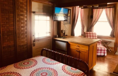 Cozy room with a bed, TV, kitchenette, and a chair, featuring warm wood tones and patterned decor.