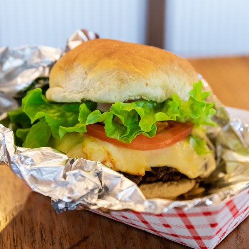 A delicious cheeseburger with lettuce, tomato, and melted cheese, wrapped in foil and served in a red-checkered container.