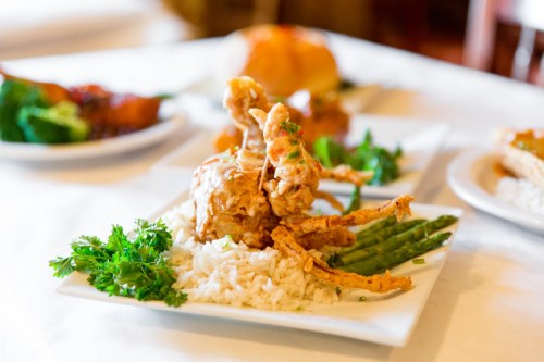 A plate of fried soft-shell crab on rice, garnished with parsley and served with asparagus, with other dishes in the background.