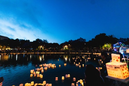 People gather by a lake at dusk, releasing glowing lanterns that float on the water's surface.
