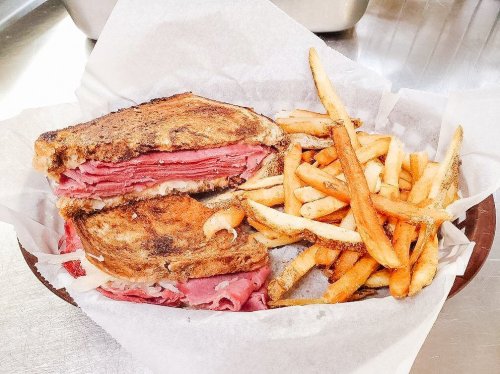 A grilled sandwich filled with layers of meat, served with a side of crispy French fries in a basket.