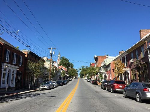 A quiet street lined with brick buildings and parked cars under a clear blue sky.