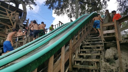 A group of children and teens climbing stairs to a water slide at a park on a sunny day.