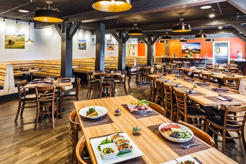 A spacious restaurant interior with wooden tables, chairs, and colorful decor, featuring dishes on tables.