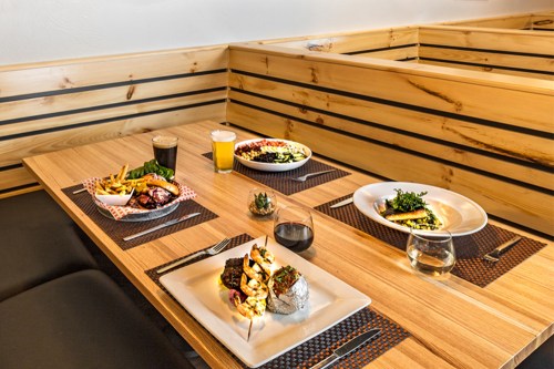 A wooden table set with various dishes, including grilled shrimp, fries, and drinks, in a cozy dining space.