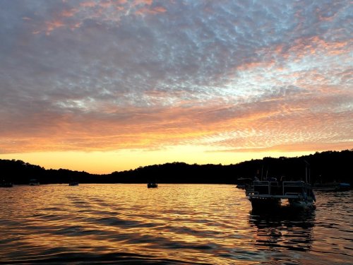 A serene sunset over a lake, with colorful clouds reflecting on the water and boats gently floating.