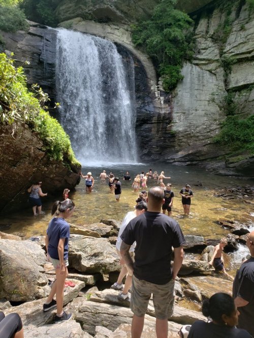 A group of people enjoying a sunny day at a waterfall, with some swimming and others relaxing on the rocks.