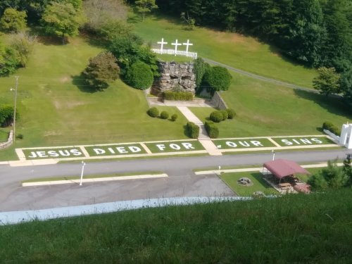A grassy area with large white letters spelling "JESUS DIED FOR OUR SINS" and three crosses in the background.