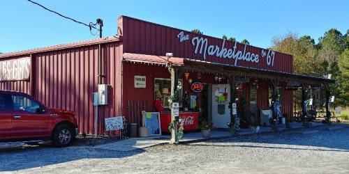 A red metal building with a sign reading "The Marketplace '67," featuring an open sign and outdoor decorations.