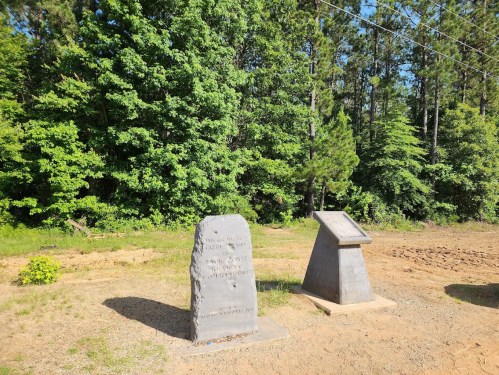 Two stone monuments stand in a clearing surrounded by dense green trees and underbrush.