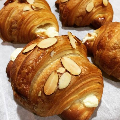 Freshly baked almond croissants with creamy filling, topped with sliced almonds, on a parchment-lined surface.