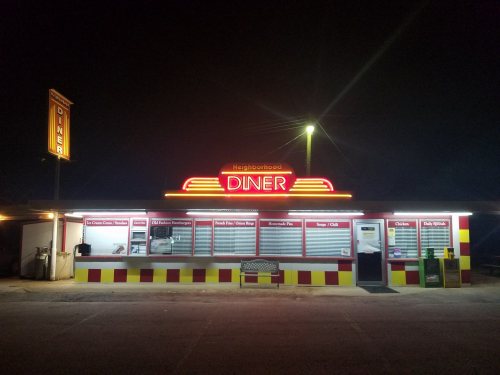 A brightly lit diner at night with neon signage, featuring a colorful exterior and menu displayed in windows.