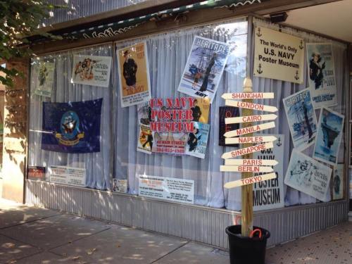 A storefront window displaying various U.S. Navy posters and a signpost pointing to different cities around the world.