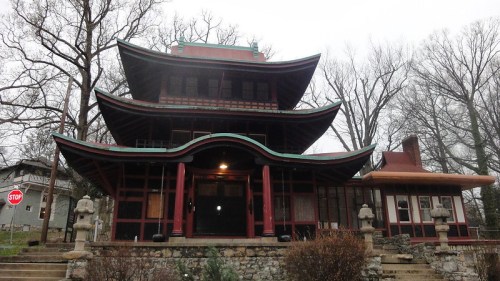 A multi-tiered, Asian-inspired building with a curved roof, surrounded by trees and a stop sign nearby.
