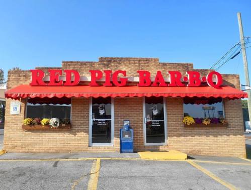 Exterior of Red Pig Bar-B-Q restaurant with a red awning and colorful flower planters.