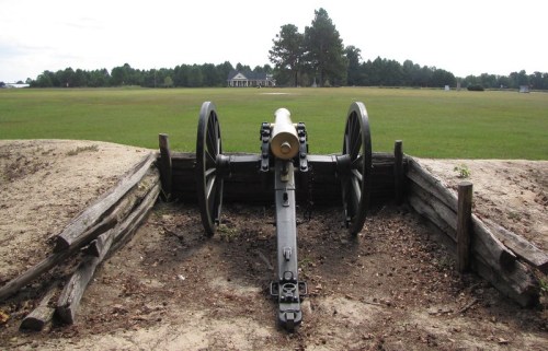 A historic cannon positioned in a grassy field, overlooking a distant house and trees.