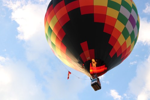 A colorful hot air balloon with a flame visible, soaring against a blue sky with scattered clouds.