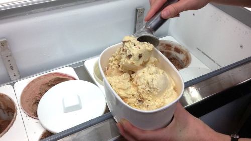 A person scoops ice cream from a container, holding a tub filled with creamy, light-colored ice cream.