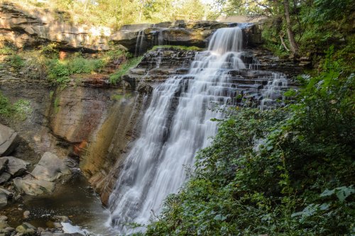 A cascading waterfall surrounded by lush greenery and rocky cliffs, creating a serene natural scene.
