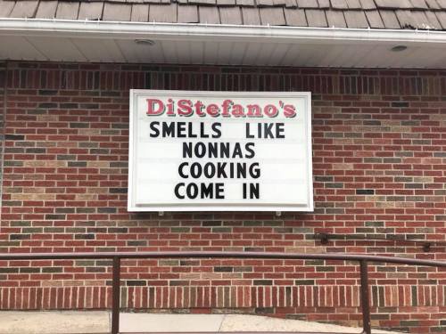 Sign outside DiStefano's reads: "Smells like Nonna's cooking. Come in." on a brick wall.