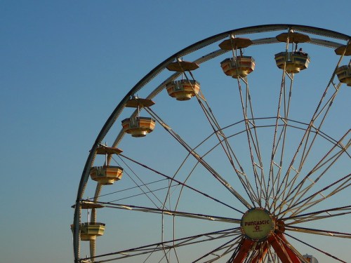 A close-up of a Ferris wheel against a clear blue sky, showcasing its colorful cabins and structure.