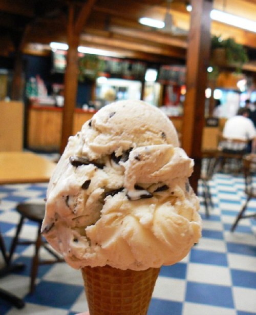 A close-up of a cone filled with chocolate chip ice cream, set against a cozy, rustic ice cream shop interior.