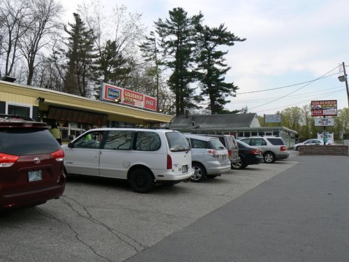 A parking lot with several cars in front of a restaurant, surrounded by trees and signs for nearby businesses.