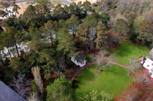 Aerial view of a green lawn surrounded by trees, with a small white house and winding path visible.