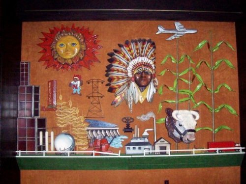 Colorful mural featuring a sun, Native American headdress, corn, a cow, and industrial elements against an orange background.