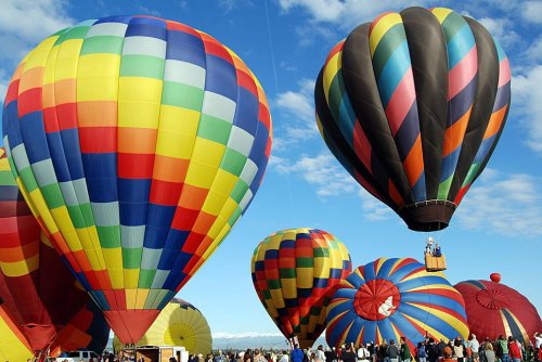 Colorful hot air balloons fill the sky at a festival, with people gathered below enjoying the vibrant display.