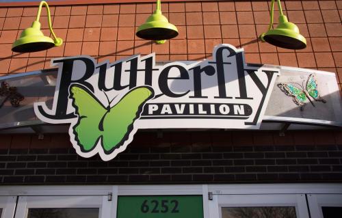 Sign for Butterfly Pavilion featuring a green butterfly and decorative elements, located on a brick building.