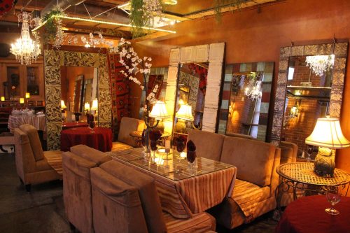 Cozy restaurant interior with plush seating, elegant mirrors, chandeliers, and warm lighting.