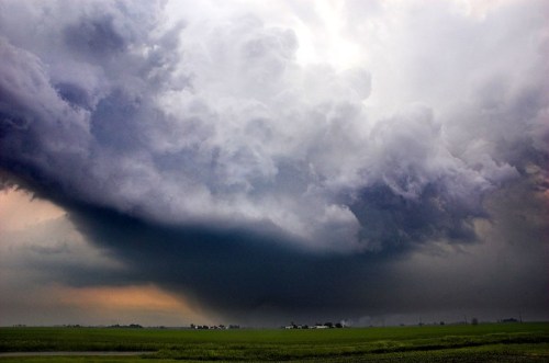 Dramatic storm clouds loom over a green landscape, hinting at an impending storm.