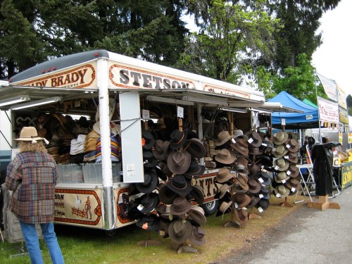 A vendor stall displaying a variety of Stetson hats, with a person browsing nearby in a plaid shirt.