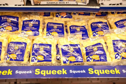 A display of Tillamook cheddar cheese curds in blue packaging, labeled with prices and "Squeek" text below.