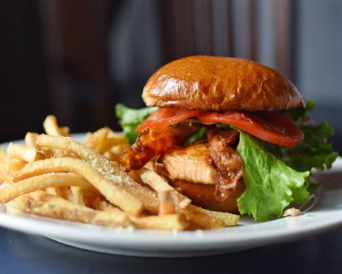 A juicy chicken sandwich with lettuce, tomato, and bacon, served with a side of crispy French fries.