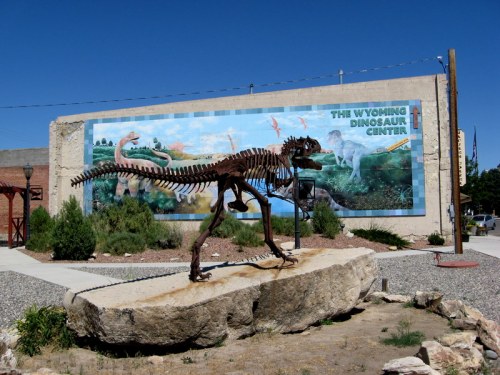 A dinosaur skeleton on a rock in front of a mural depicting dinosaurs at the Wyoming Dinosaur Center.