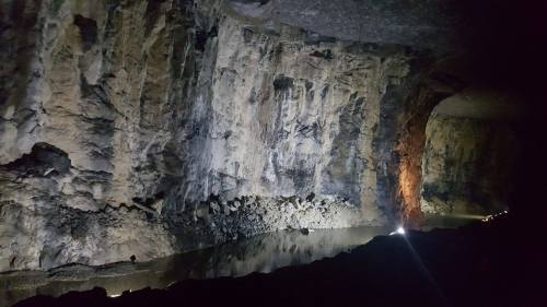 A dimly lit cave with rocky walls and a calm water surface reflecting light.