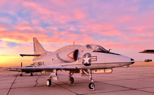A military jet on a runway at sunset, with colorful clouds in the background.