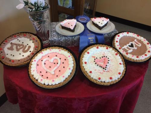 A table displays decorated cakes with heart designs, a blue ribbon, and a floral arrangement in a vase.