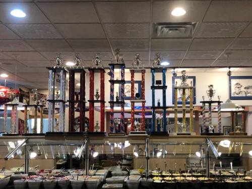 A display of tall trophies on a shelf above a buffet, with various colored columns and decorative figures on top.