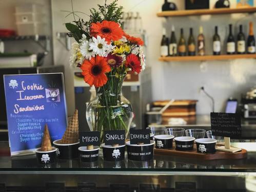 A display of cookie ice cream sandwiches with a flower vase and menu board in a cozy café setting.