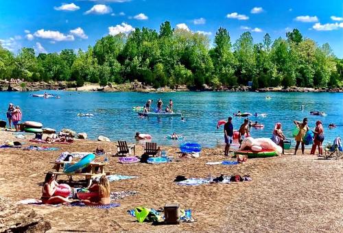 A sunny beach scene with people swimming, lounging on towels, and enjoying the water surrounded by greenery.