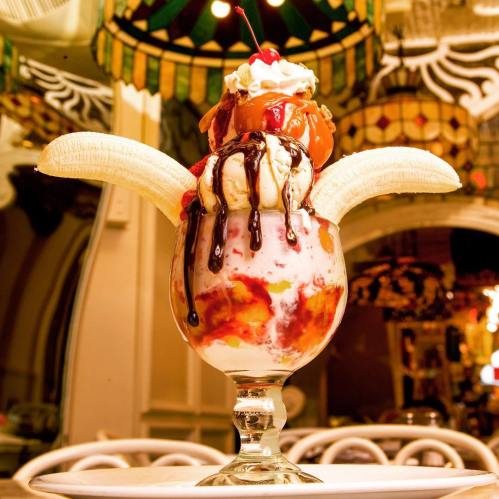 A tall glass filled with ice cream, topped with whipped cream, a cherry, chocolate syrup, and banana slices.