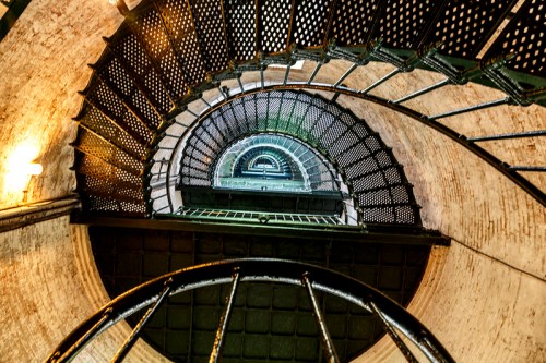 A spiral staircase viewed from above, showcasing metal steps and a circular design against a brick wall.