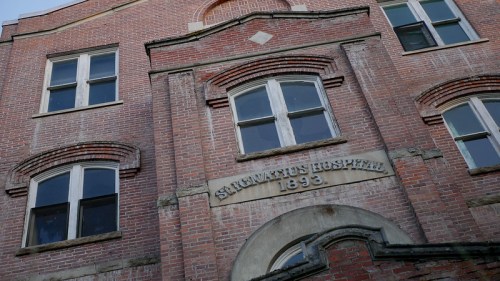 Historic brick building with large windows, featuring a sign that reads "St. Ignatius Hospital 1893."