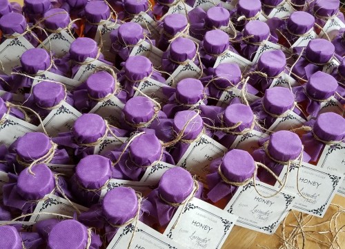 A close-up of numerous jars of honey, each with a purple lid and a decorative label, arranged neatly on a surface.