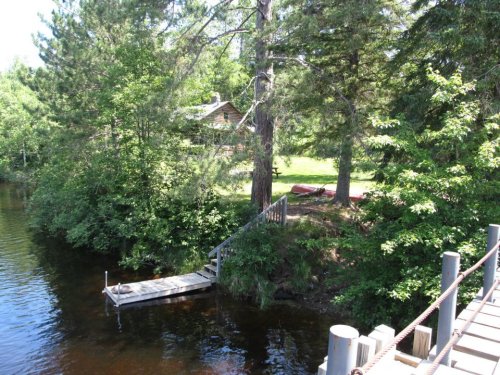 A serene lakeside scene featuring a wooden dock, lush greenery, and a cabin in the background.