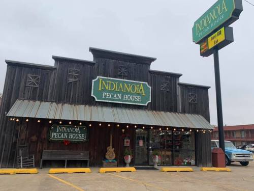 Exterior of the Indianola Pecan House, a rustic wooden building with festive lights and a sign, on a cloudy day.