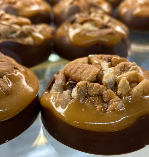 Close-up of chocolate-covered candies topped with caramel and chopped nuts, arranged neatly on a surface.